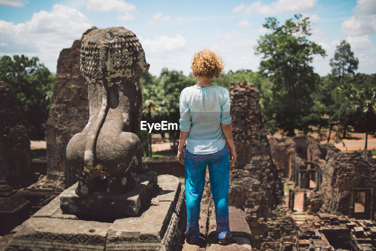 Rear view of woman standing by old statue at temple against sky