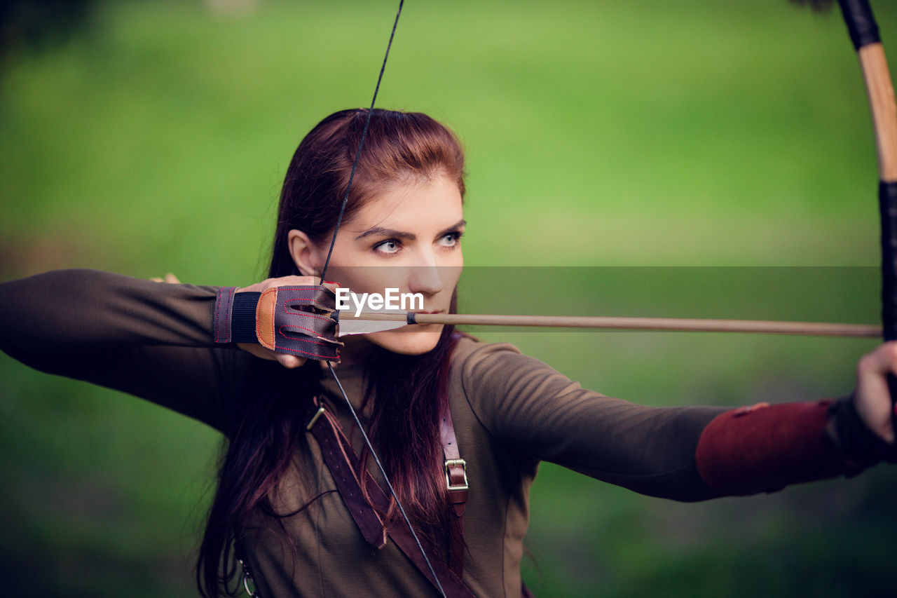 Beautiful woman holding bow and arrow standing outdoors