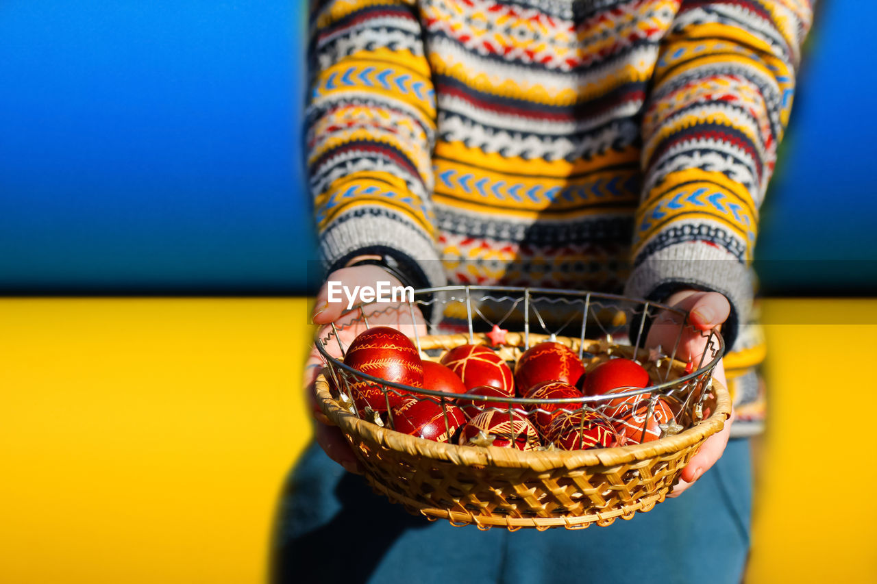 Ukrainian young smiling woman in hat holding plate of collection of red egg on nature background. 