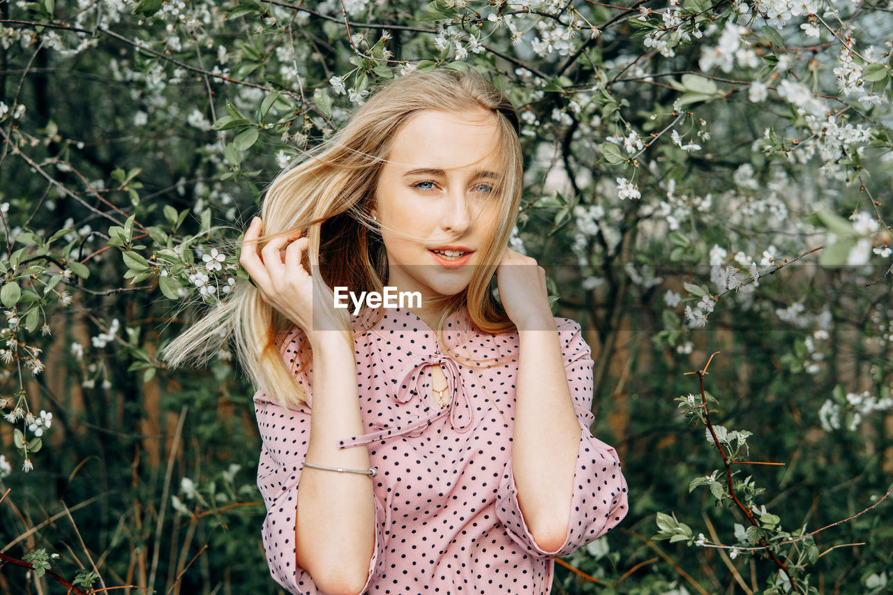 Blonde girl on a spring walk in the garden with cherry blossoms. female portrait, close-up. 