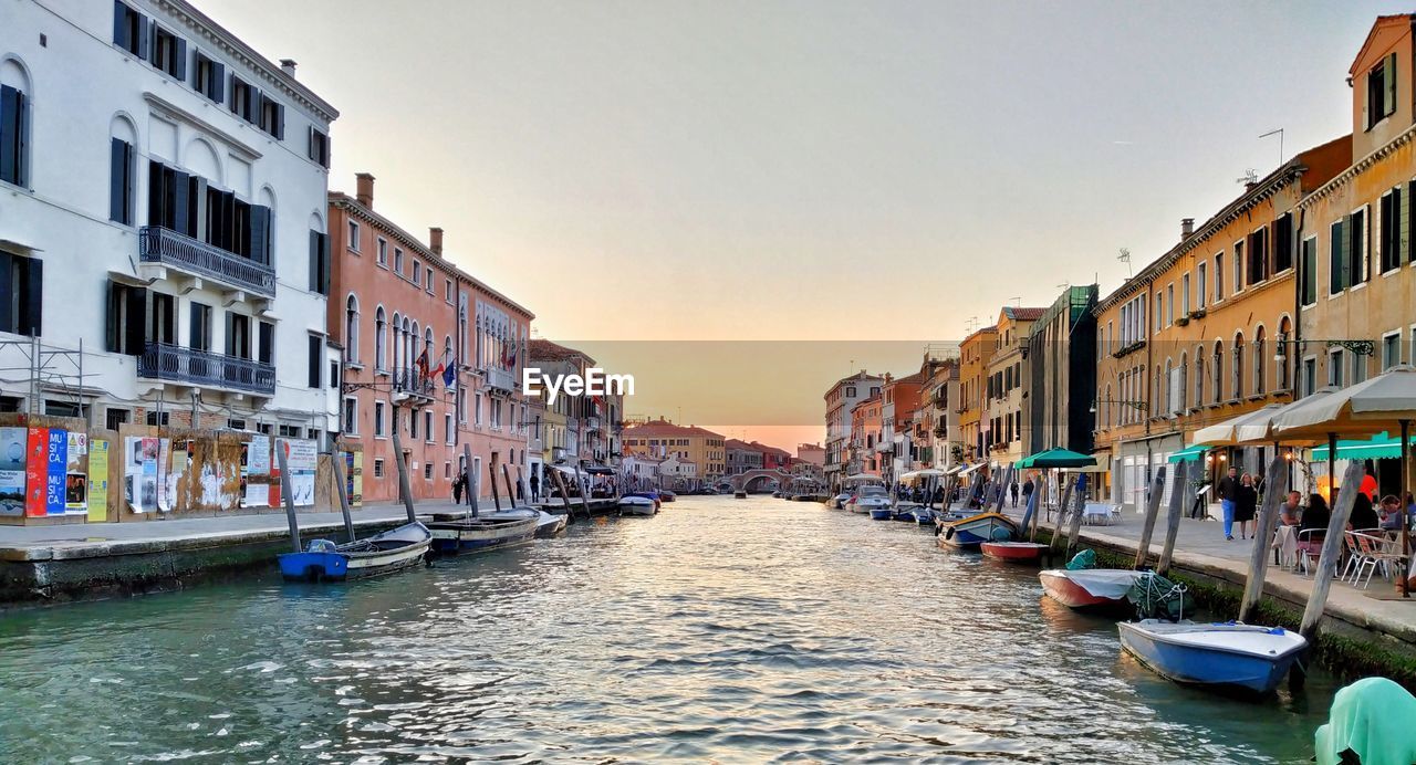 BOATS MOORED IN CANAL AMIDST BUILDINGS AGAINST SKY