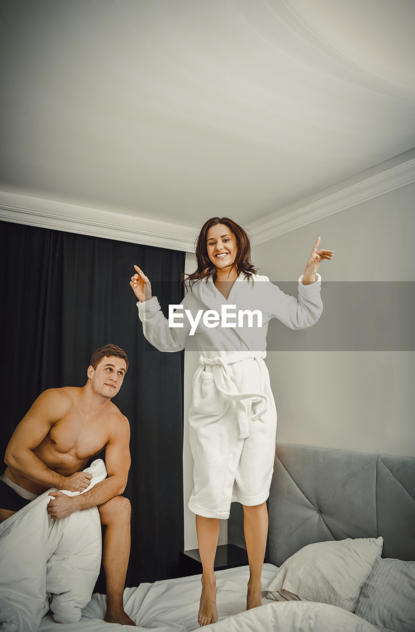 Smiling woman dancing while man holding blanket on bed at home