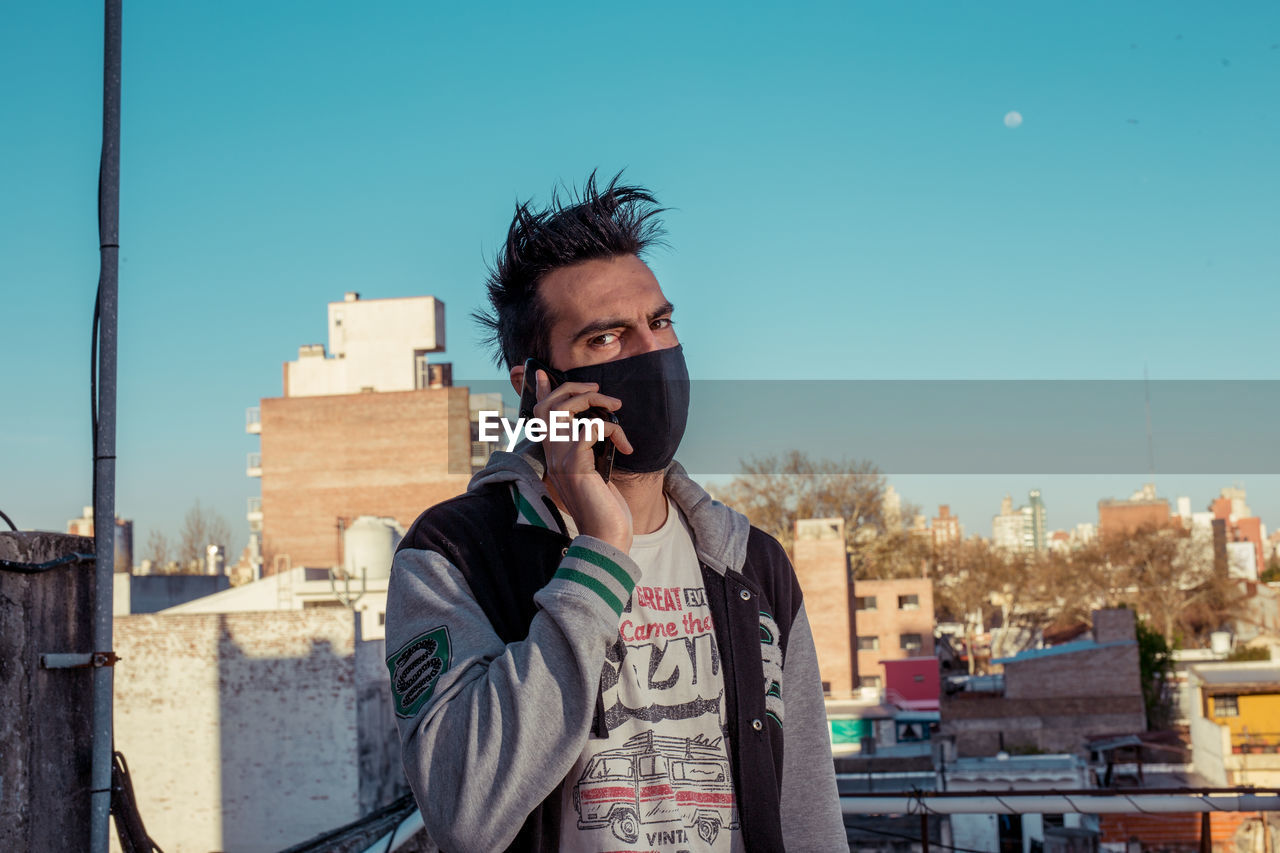 Portrait of young man with face mask in city against clear sky