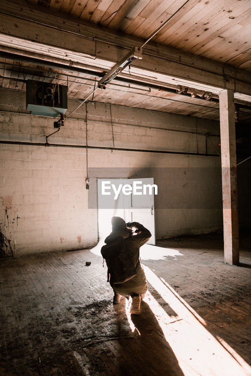 Young man with backpack crouching in abandoned room