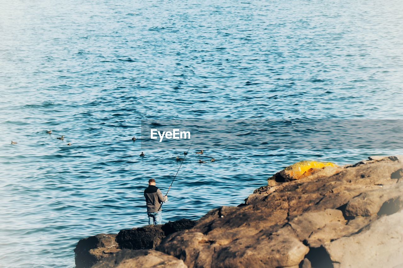 High angle view of man standing on rock by sea