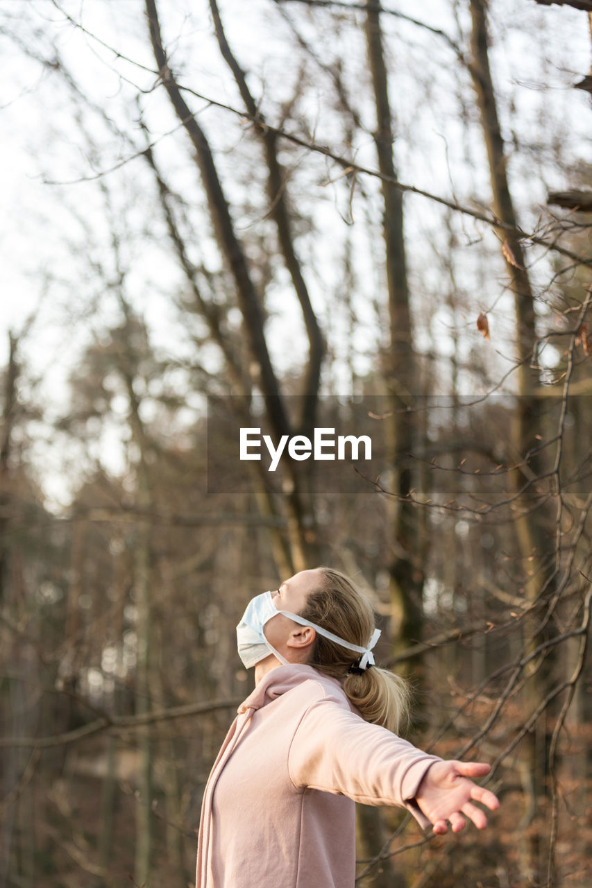 Woman wearing mask standing with arms outstretched in forest