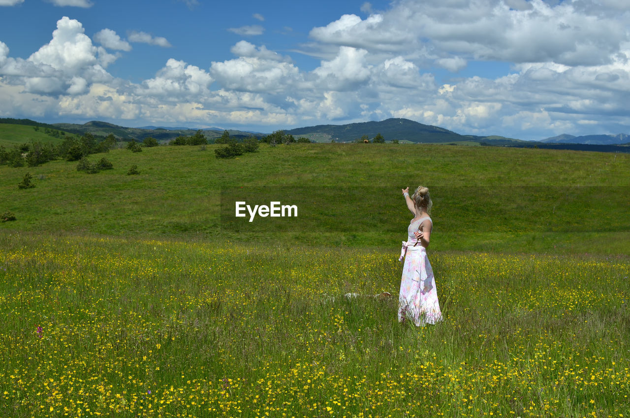 Woman showing with her hand towards hills and spring sky full of white clouds