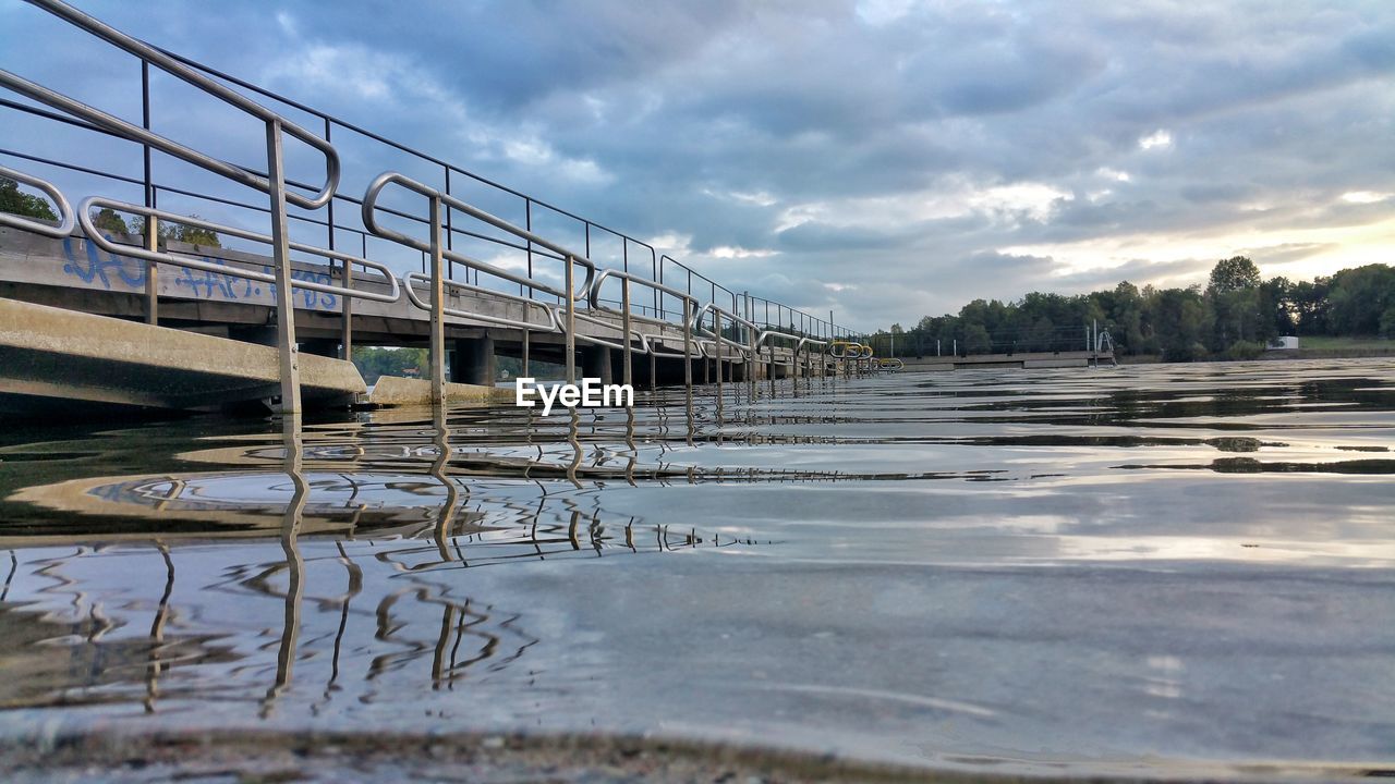 REFLECTION OF BRIDGE ON RIVER AGAINST CLOUDY SKY