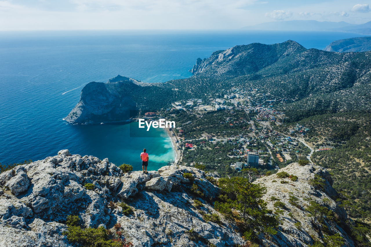 Man traveller at the top of falcon sokol mountain enjoying novyi svit town below. crimea