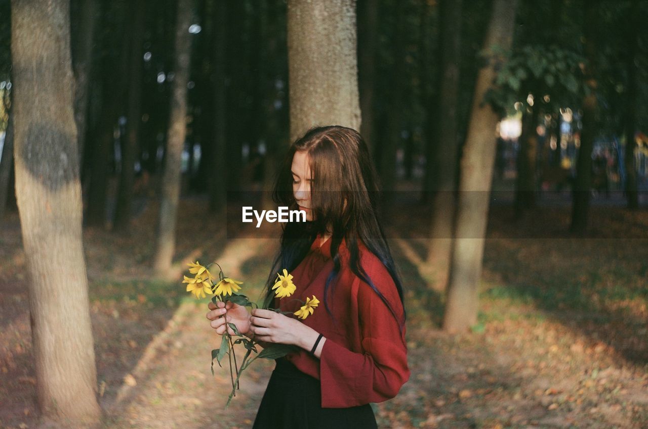 Young woman holding flowers while standing in forest