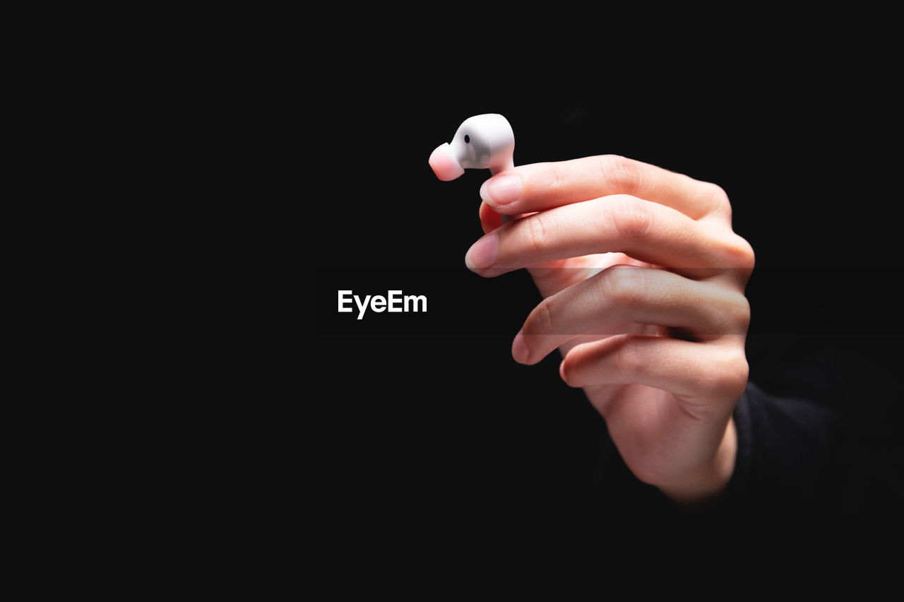 Close-up of a caucasian girl's hand with an earphone on a black background. demonstration of a