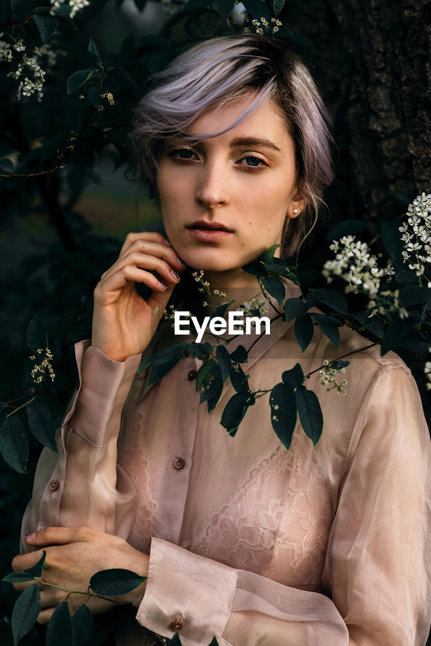 Portrait of young woman standing by plants at park