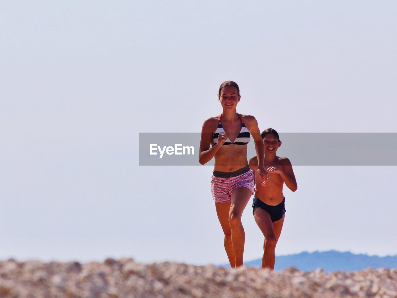 Smiling siblings running on beach against clear sky