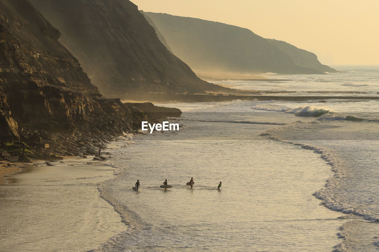 Group of surfers going to surf in the ocean at the sunset.