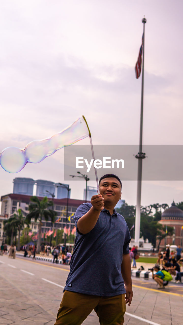 Young man with bubble wand against sky