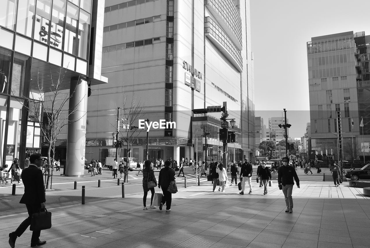 PEOPLE WALKING ON STREET IN CITY AGAINST SKY