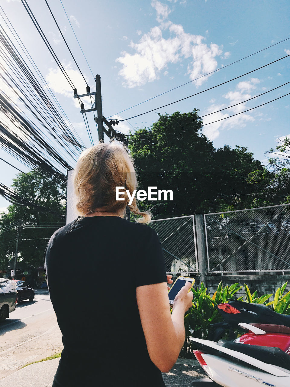 REAR VIEW OF WOMAN STANDING BY CABLE AGAINST SKY