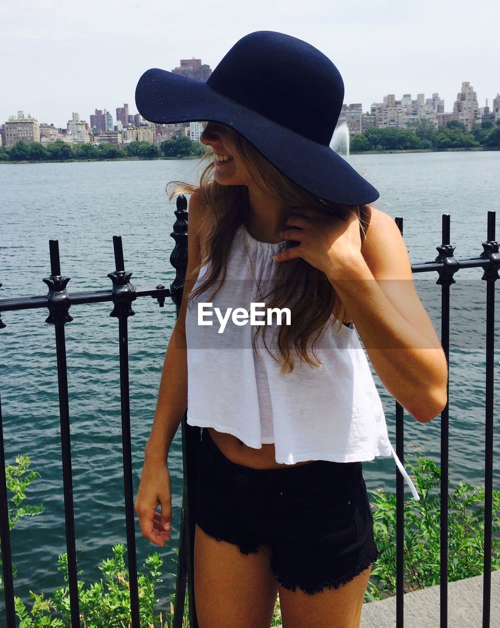 Young woman wearing hat while standing against river