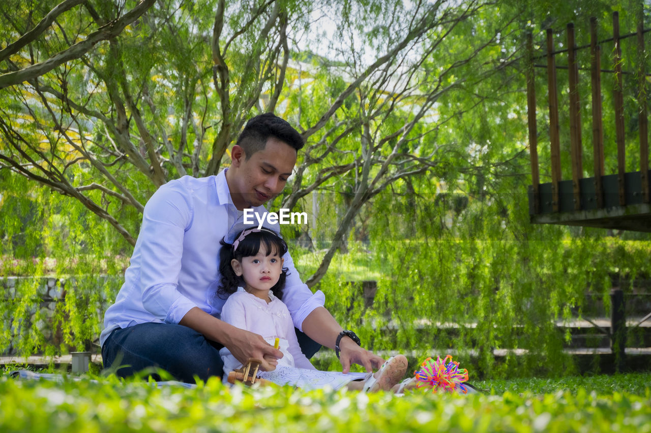 Full length of father and daughter sitting on grass outdoors