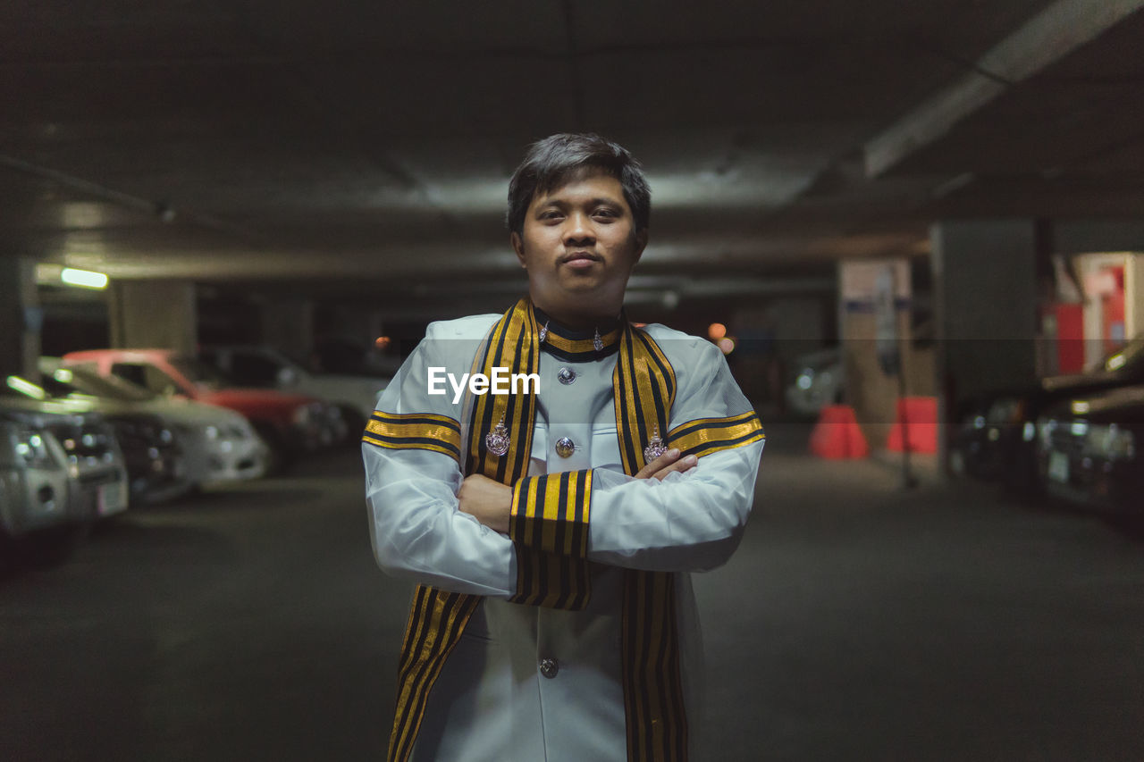 Portrait of young man with arms crossed standing at parking lot