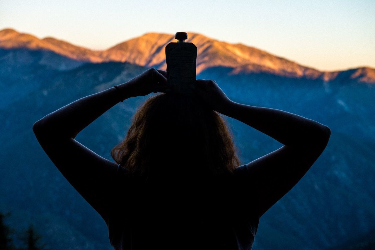 Silhouette woman holding bottle on head against mountains