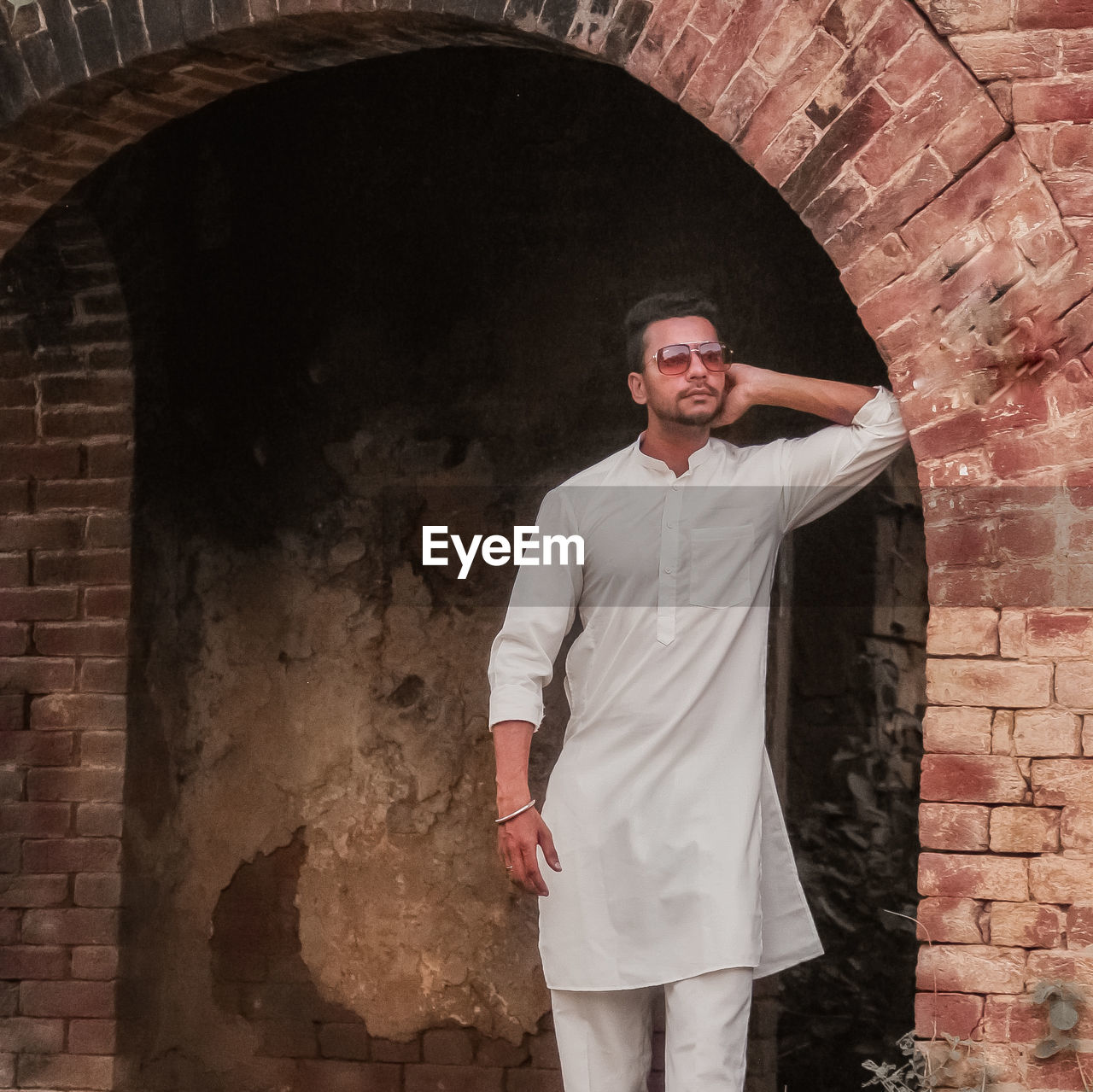 PORTRAIT OF MAN STANDING AGAINST BRICK WALL