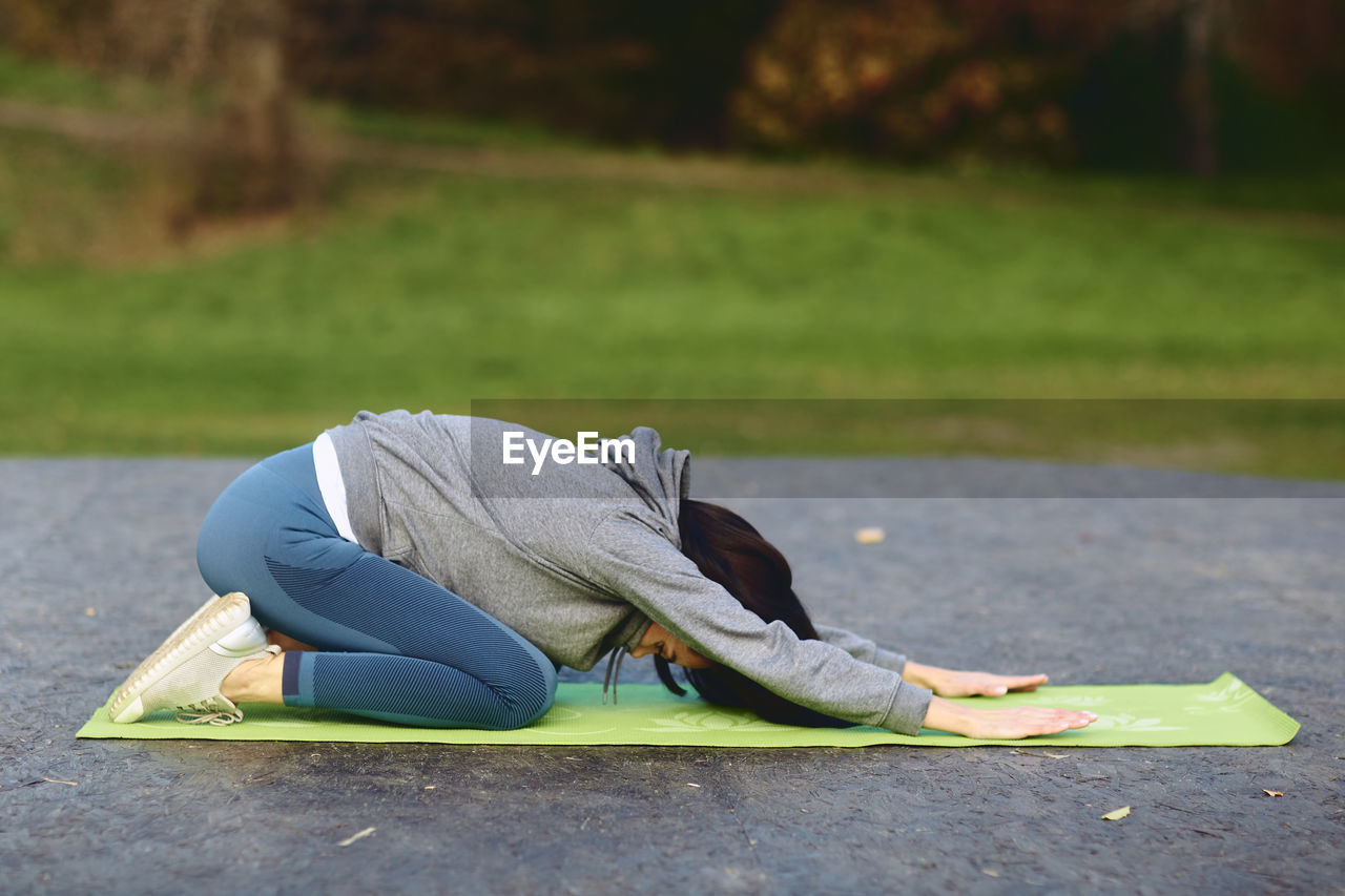 A brunette girl in a tracksuit performs morning sports exercises on yoga mat.