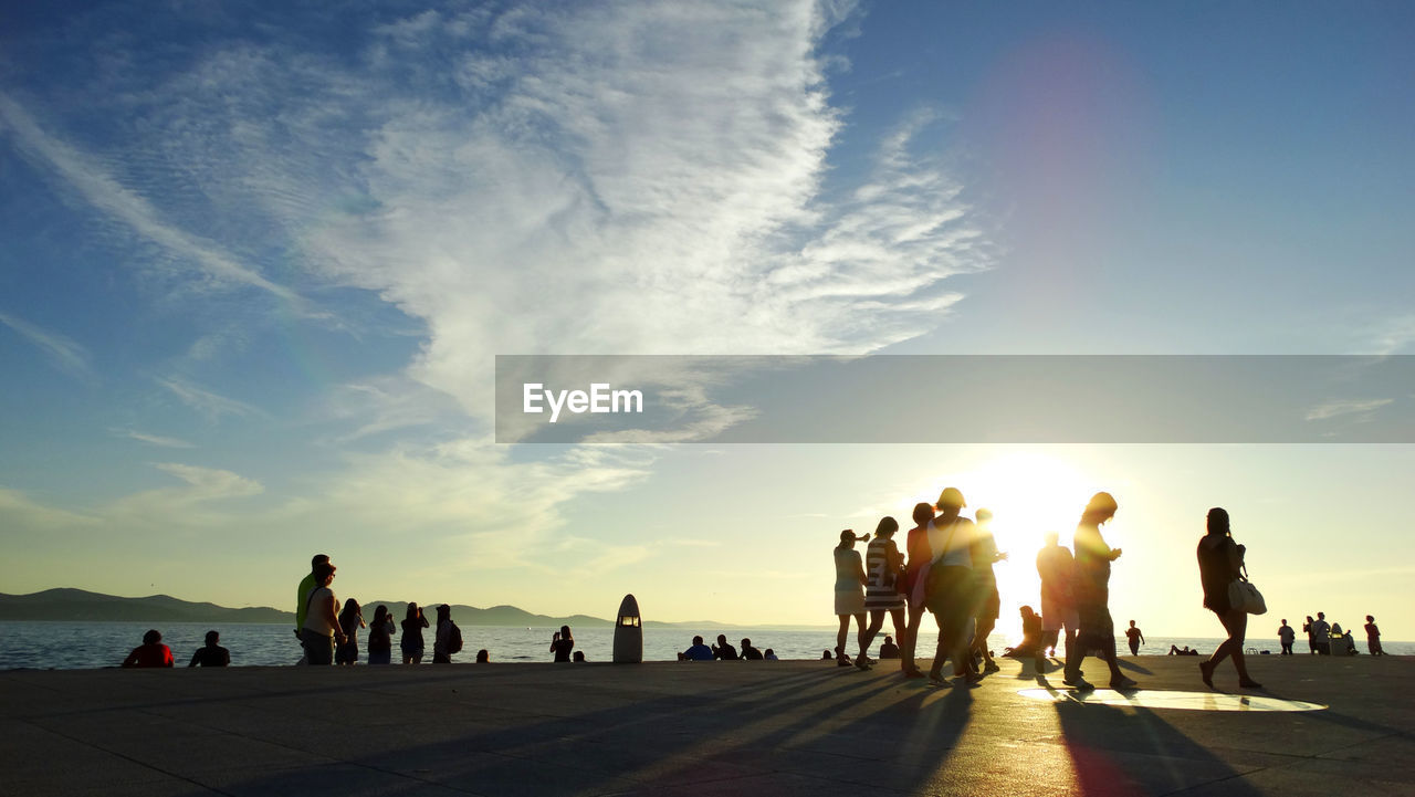 People at beach against sky during sunset