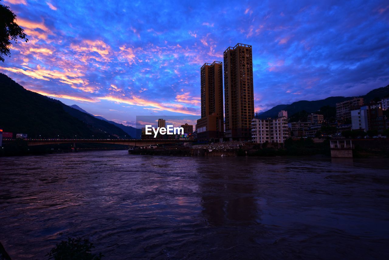 RIVER BY BUILDINGS AGAINST SKY AT NIGHT