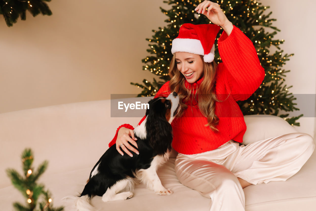 A happy girl in sweater and santa hat plays and cuddles with a pet dog during the christmas holidays