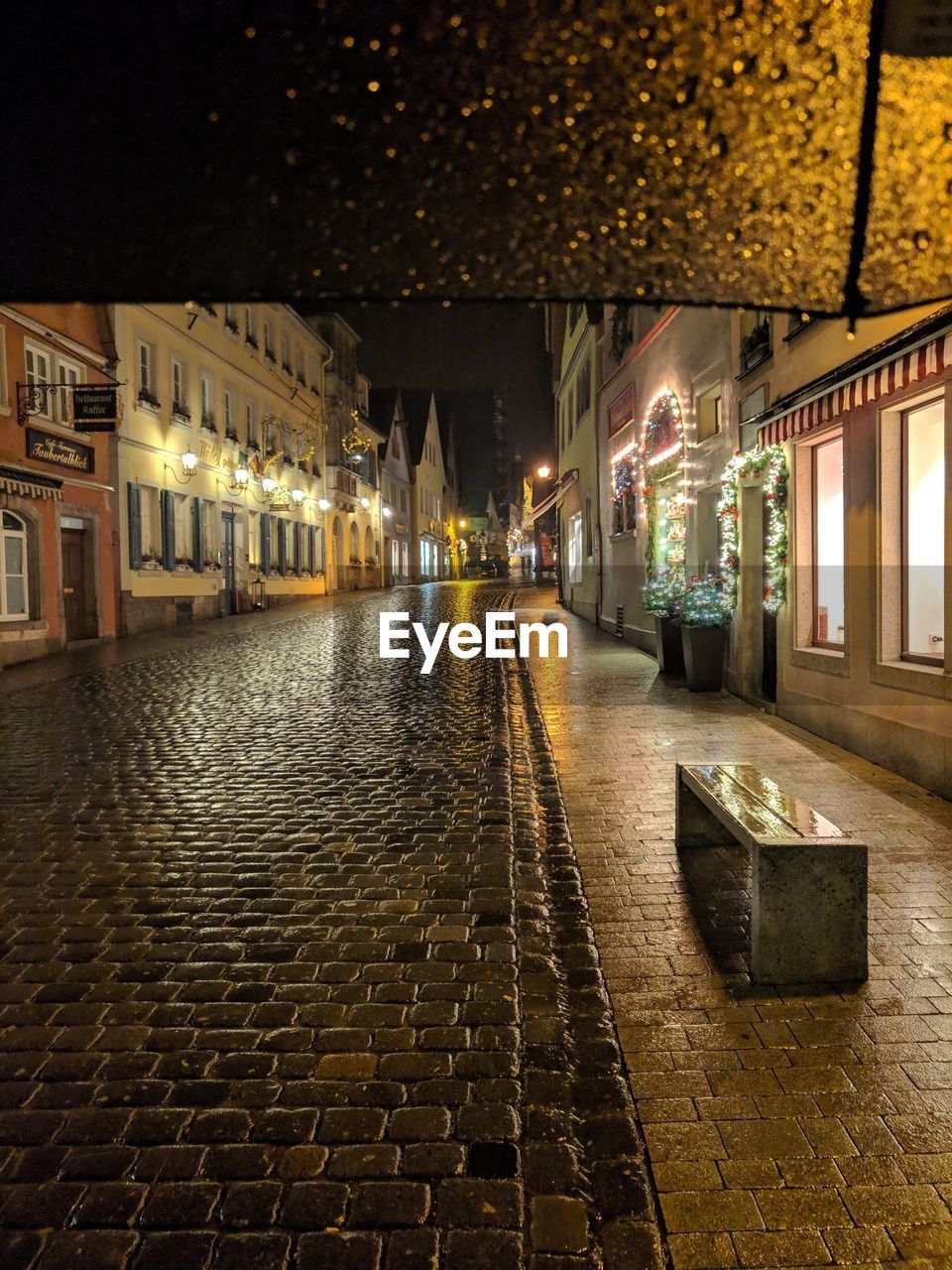 Illuminated street amidst buildings in city during rain at night