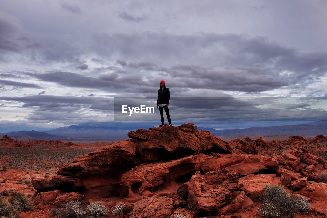 Woman standing on rock formation against cloudy sky