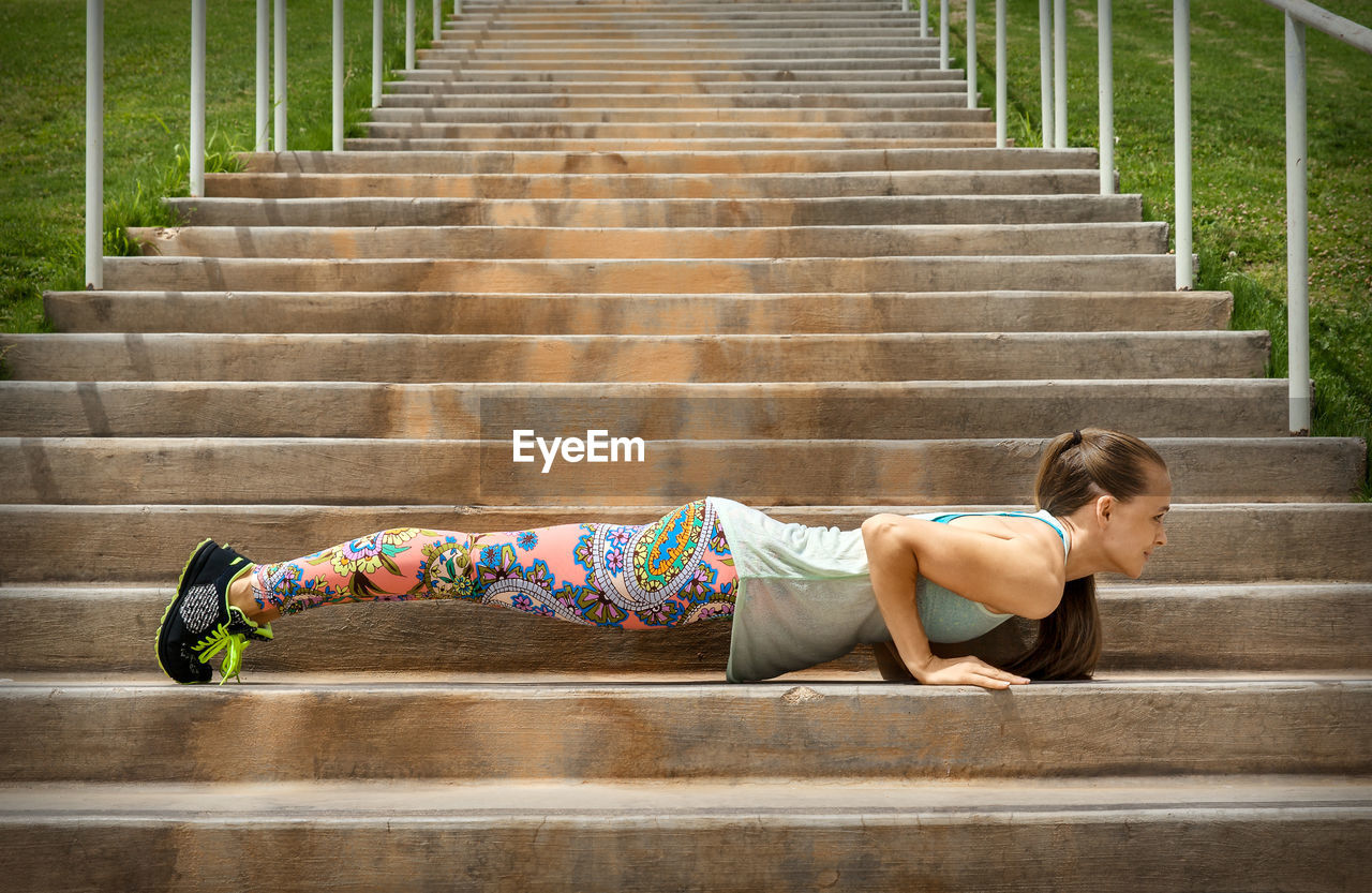 Side view full length of young woman exercising on steps