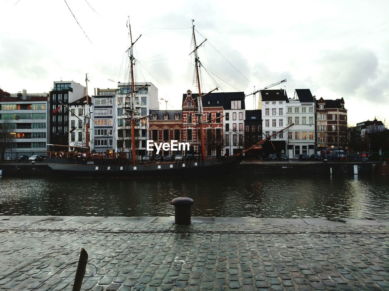 BOATS MOORED ON CITY BY RIVER AGAINST SKY IN BACKGROUND