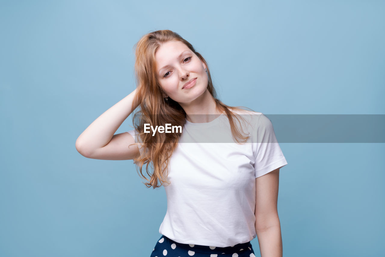 one person, studio shot, portrait, smiling, happiness, blue, casual clothing, women, long hair, hairstyle, emotion, colored background, photo shoot, young adult, looking at camera, adult, blue background, indoors, standing, cheerful, teenager, blond hair, t-shirt, front view, copy space, smile, teeth, clothing, positive emotion, waist up, child, brown hair, fashion, enjoyment, relaxation, lifestyles, sleeve, three quarter length, person, joy, looking, fun, finger, female, human hair, vitality, carefree, gray, cute