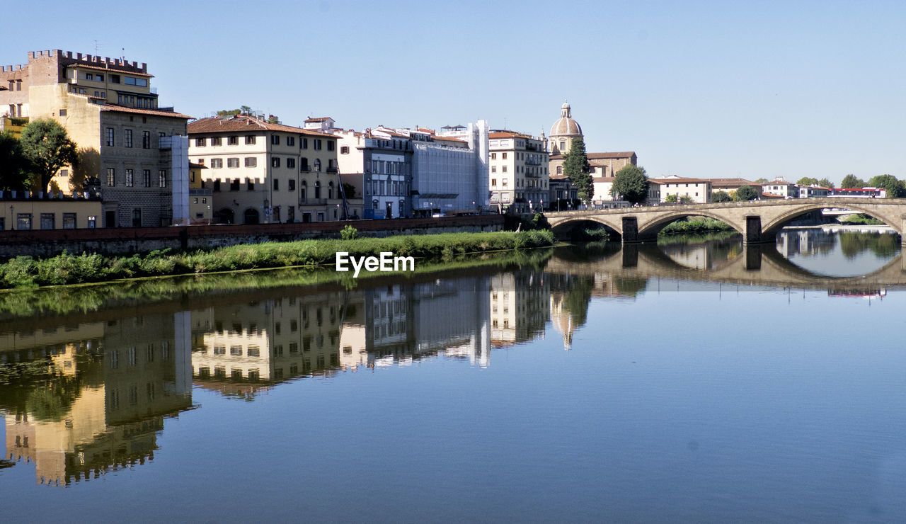 Reflection of buildings and bridge on arno river against sky