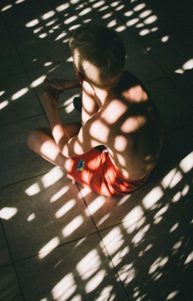 High angle view of a shirtless boy sitting on tiled floor
