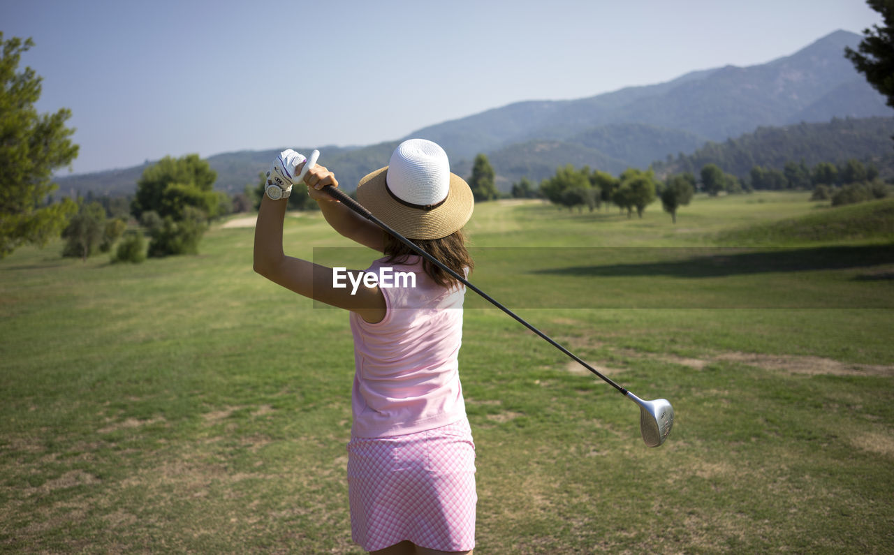 Rear view of woman wearing hat playing golf on field