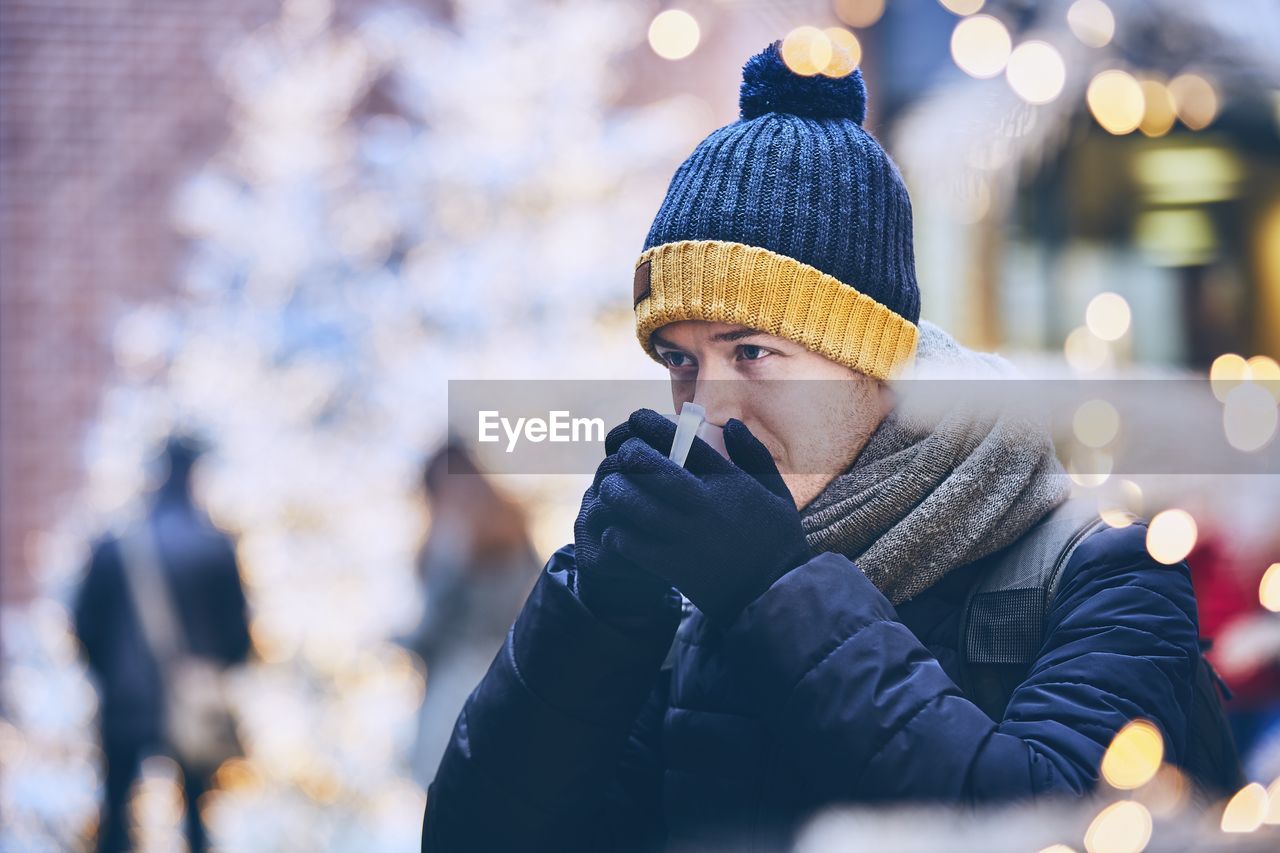 Man having drink while standing in city during winter