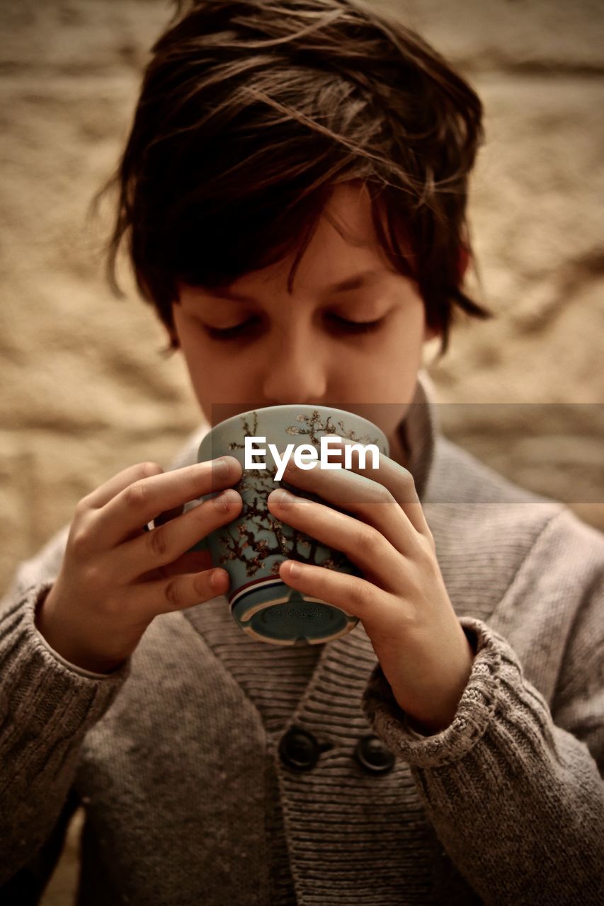 Close-up of boy wearing warm clothing while holding cup