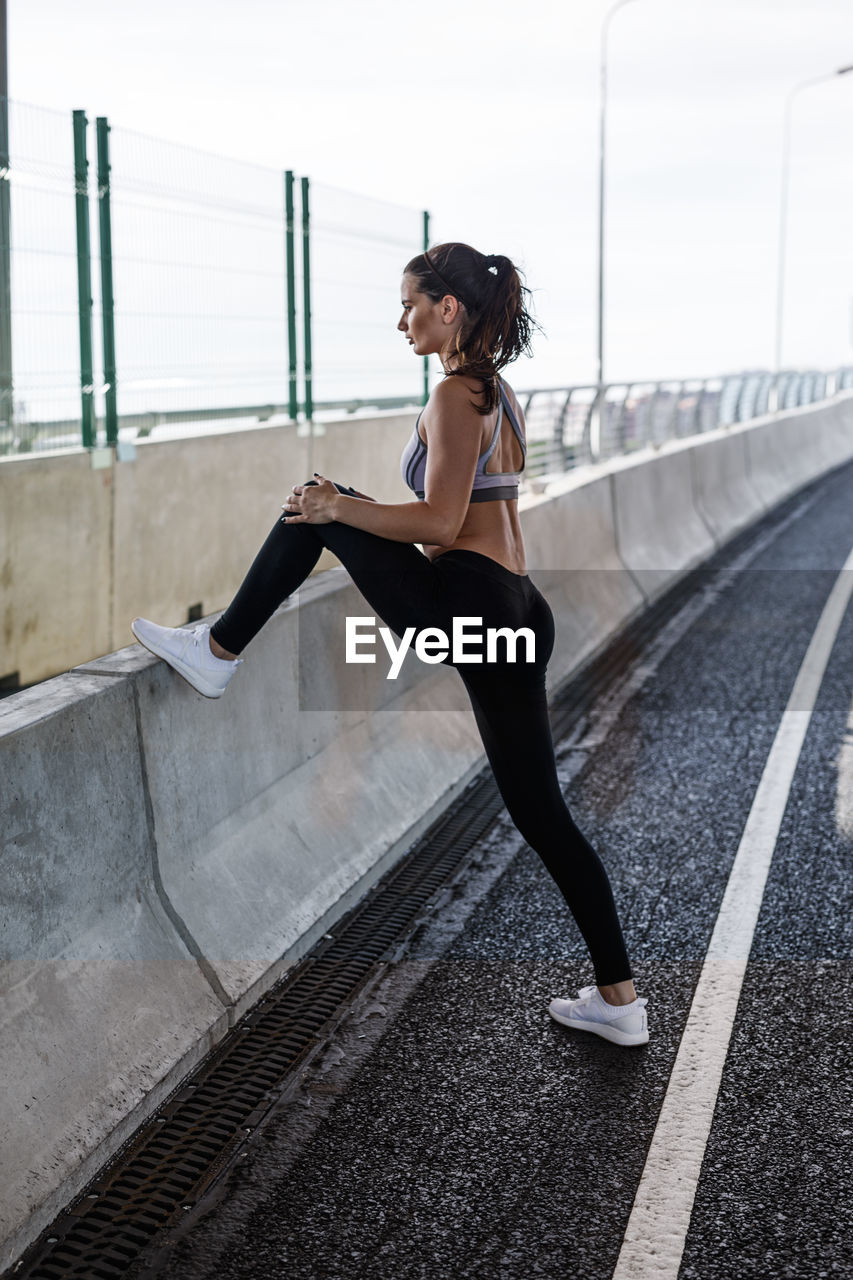 Full length of young woman exercising on bridge against sky