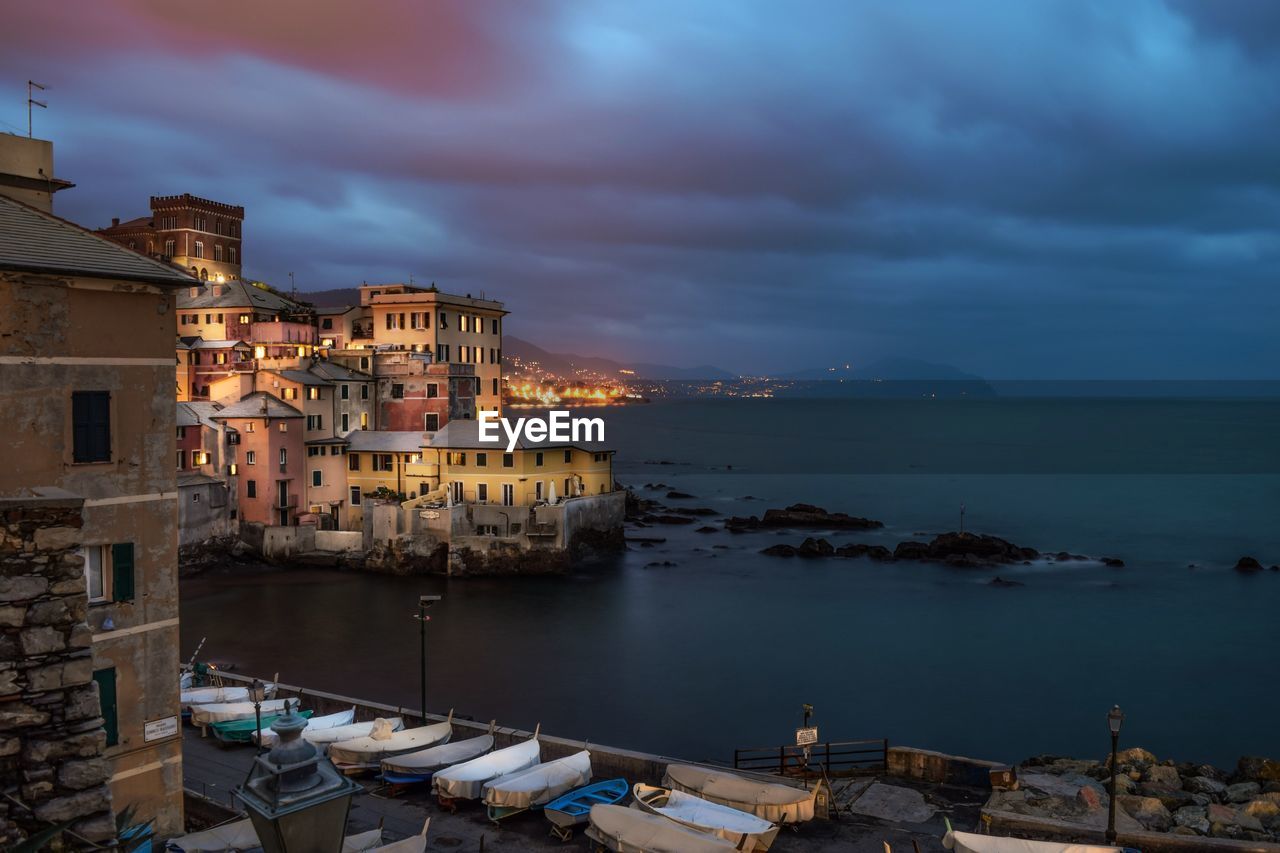 Scenic view of sea and houses against cloudy sky at dusk