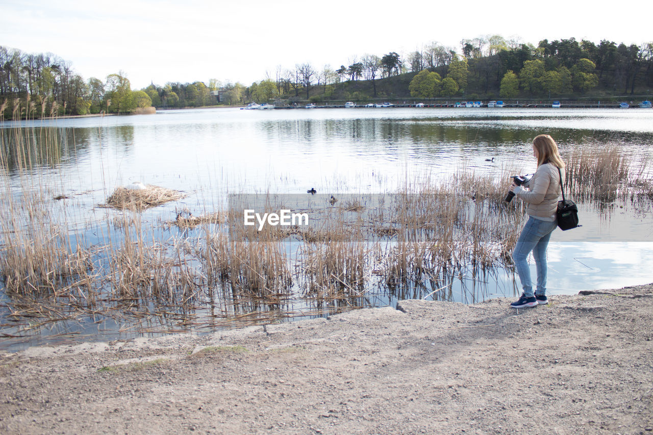 WOMAN STANDING AT LAKE AGAINST SKY