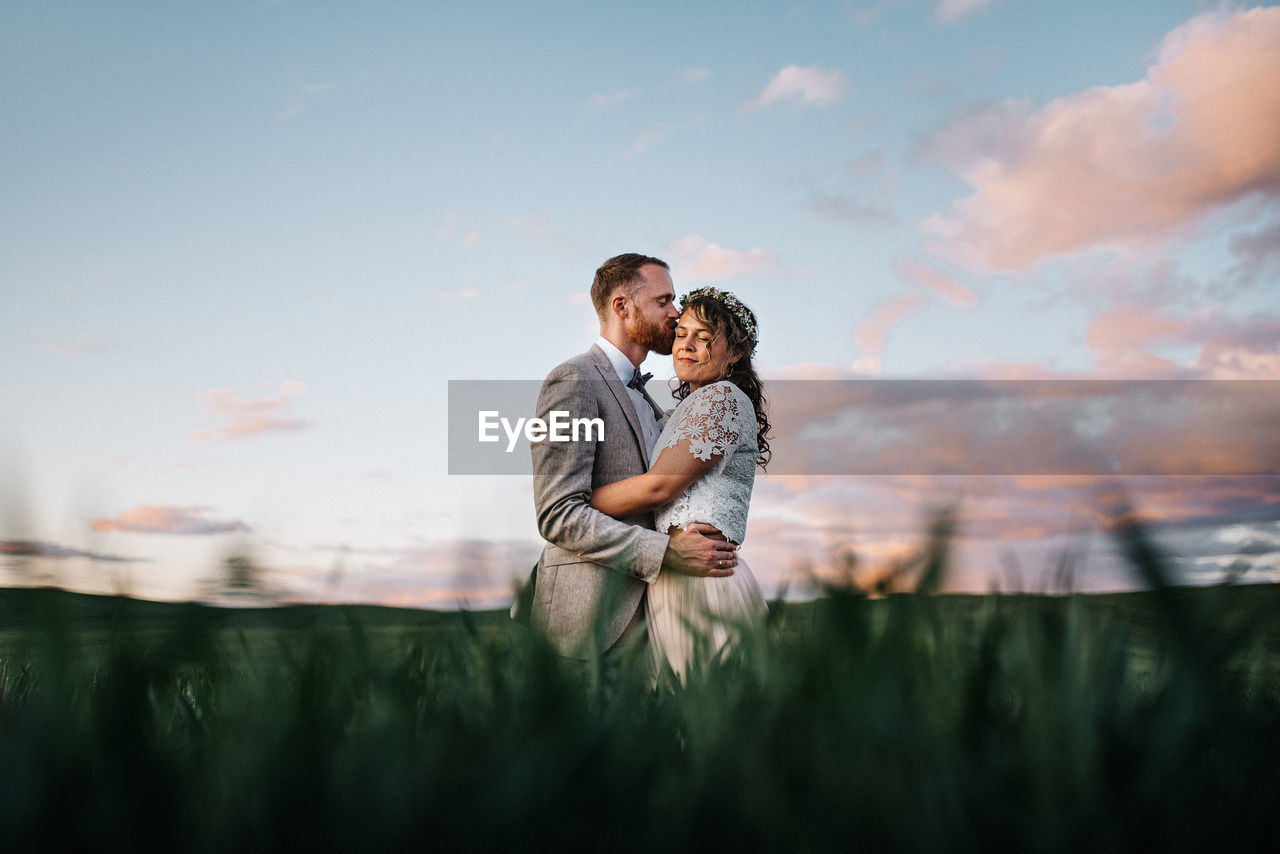 SIDE VIEW OF COUPLE KISSING AGAINST SKY AT PARK