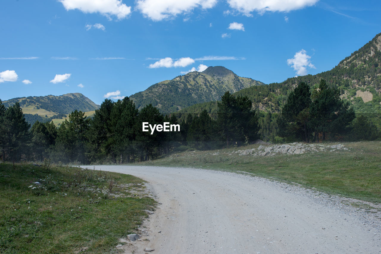 Road amidst trees and mountains against sky