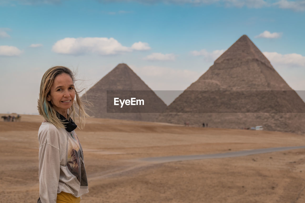 Portrait of woman standing in desert against pyramids and sky