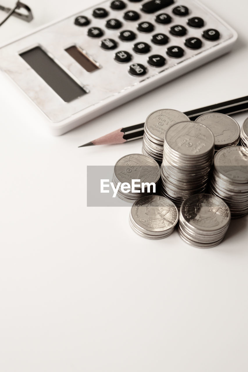 High angle view of coins with calculator and pencil on white background