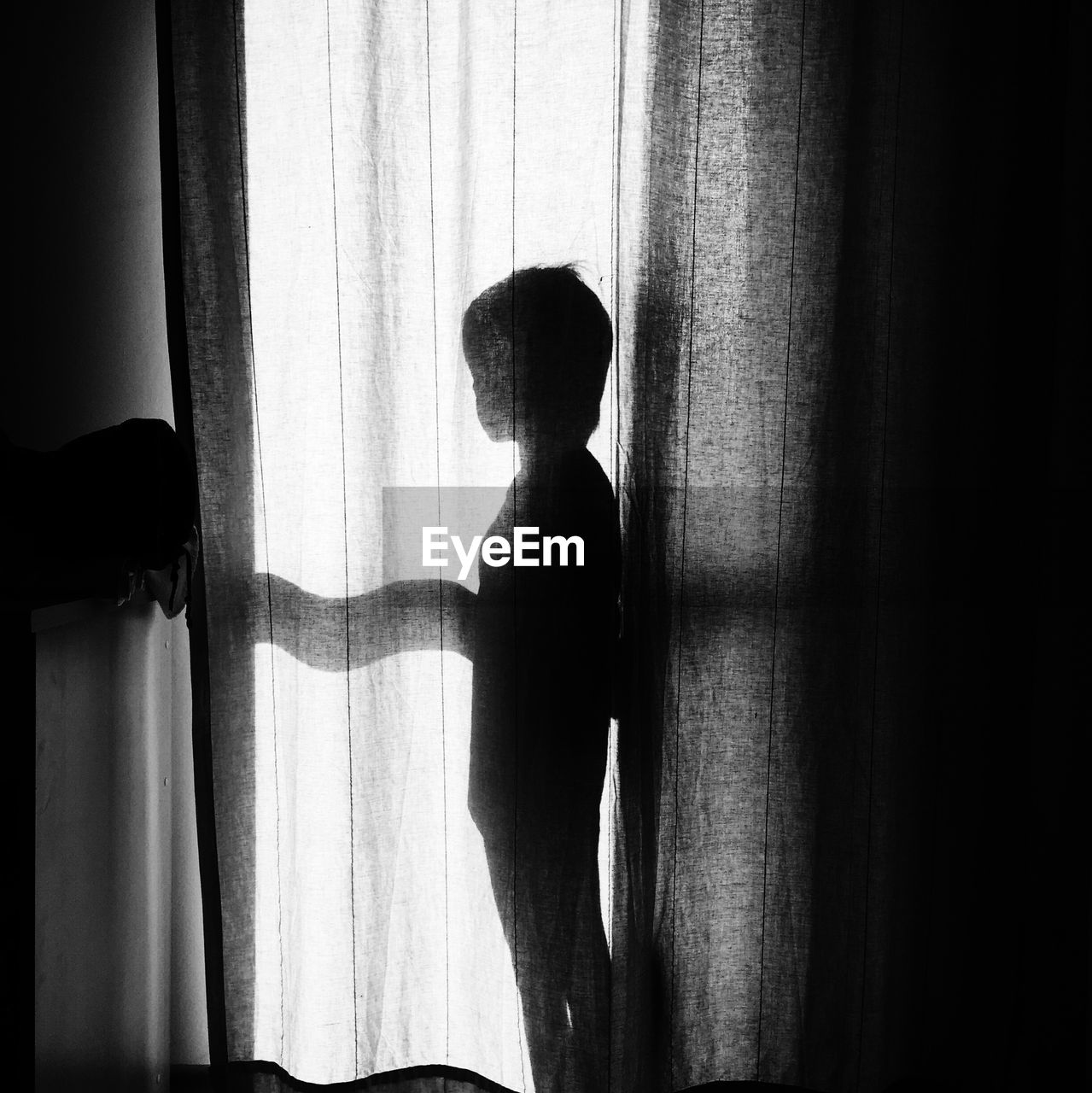 Silhouette boy standing behind curtain at home