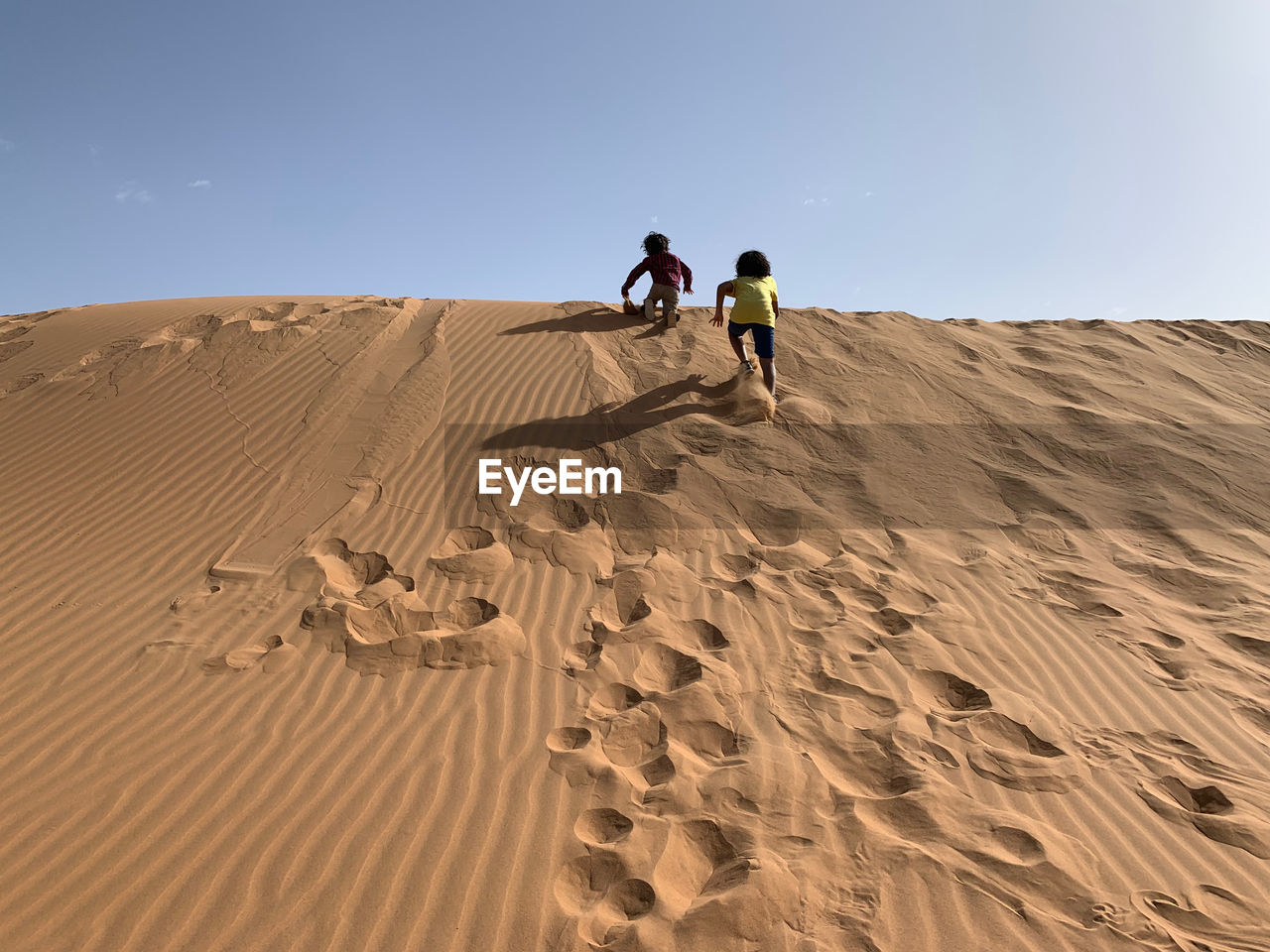 Kids walking on sand dune in desert against sky