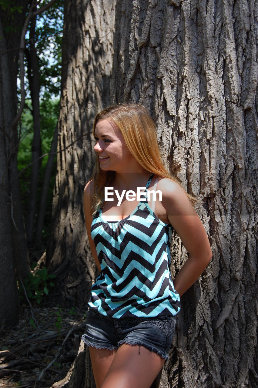 Young woman leaning on tree trunk